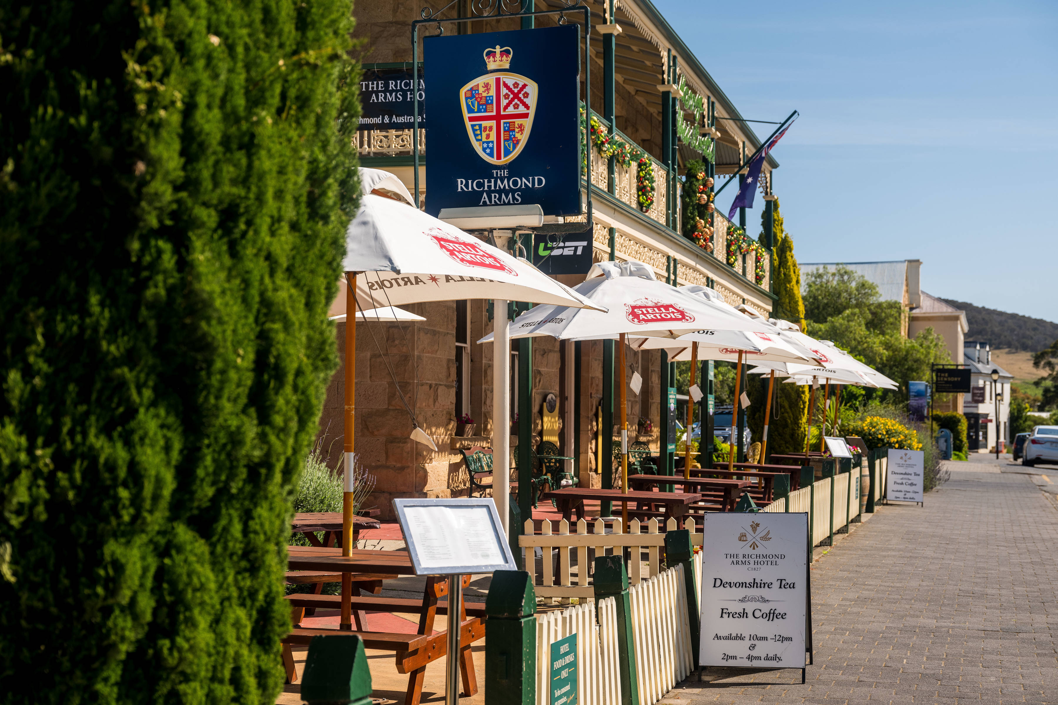 Outside view of the Richmond Arms Hotel facing Bridge Street, Richmond, showing outdoor seating and shade umbrellas on a sunny day.